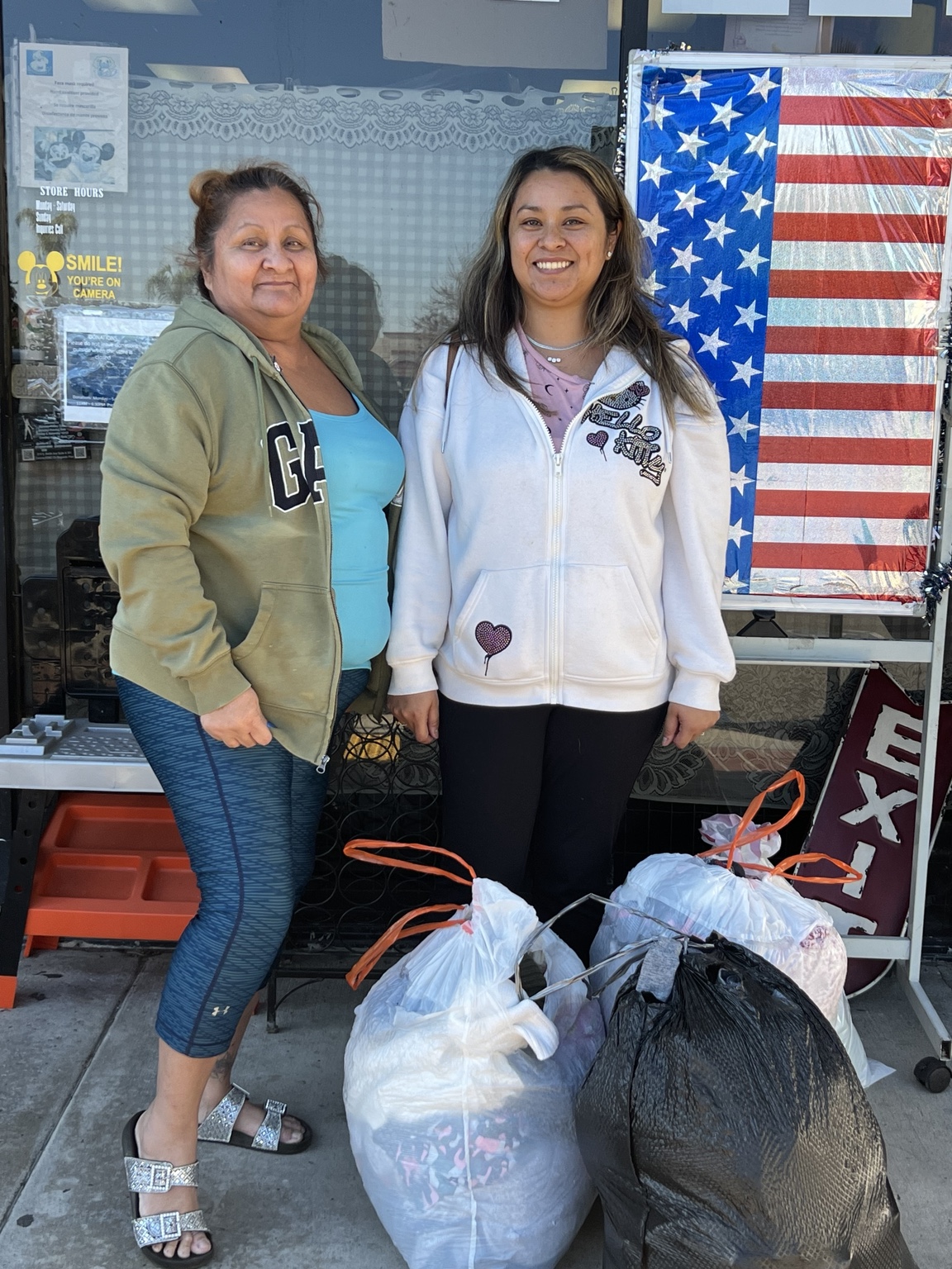 Two community members outside the thrift shop beside bags of items