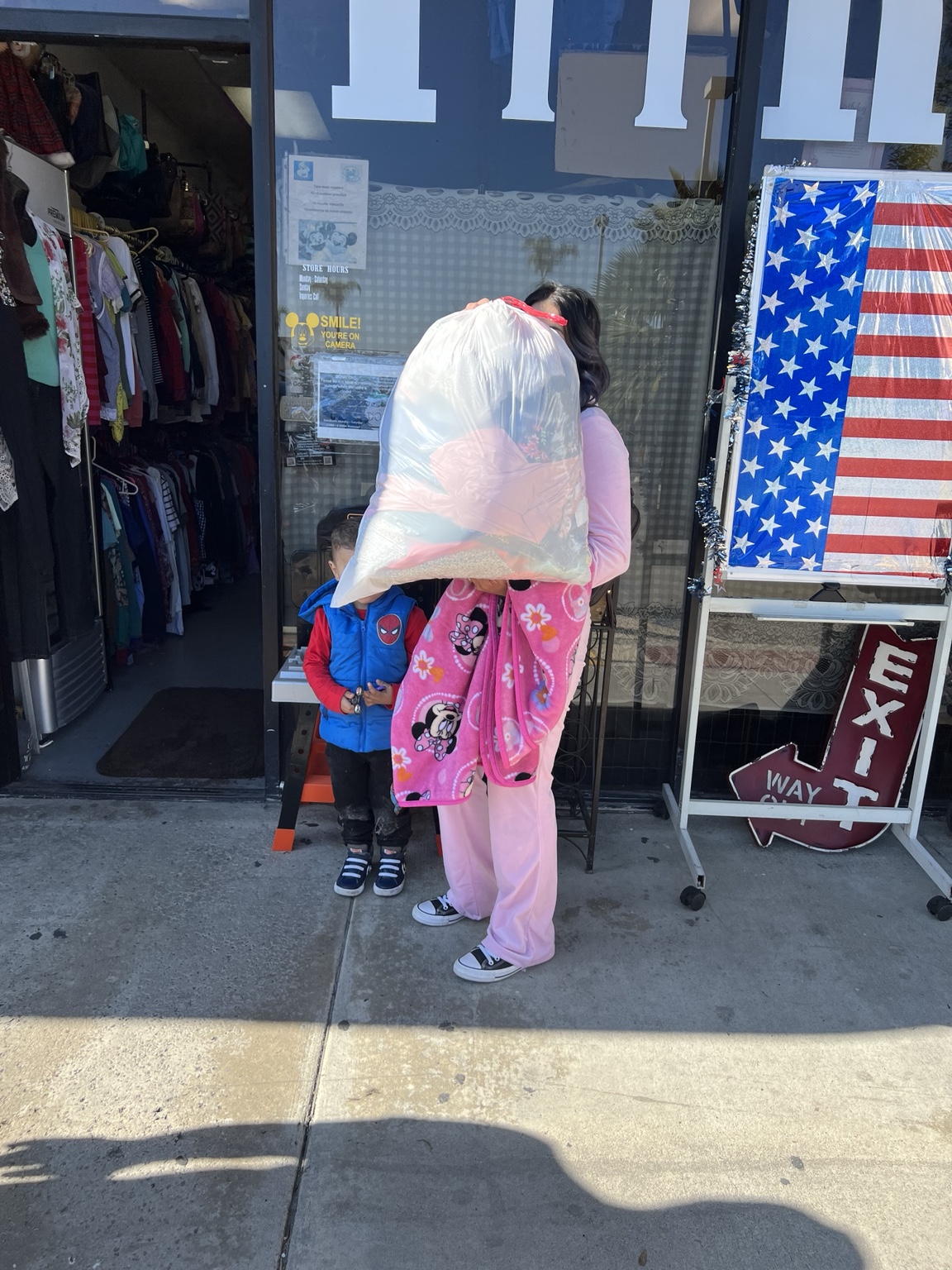 A recipient holding a bag of items in front of their face outside the thrift shop